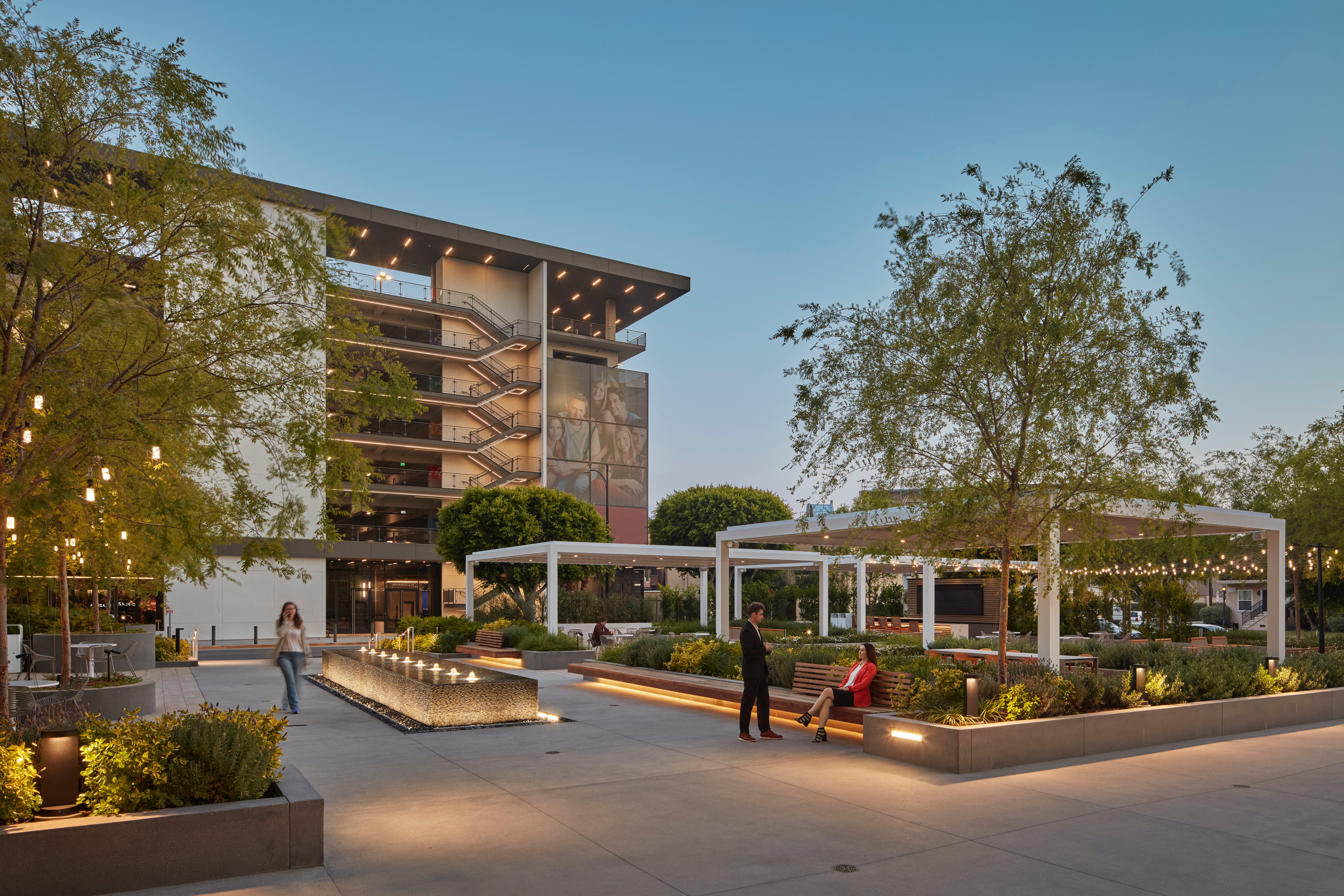Studio Plaza courtyard at dusk with water feature, string lights, and people relaxing on benches