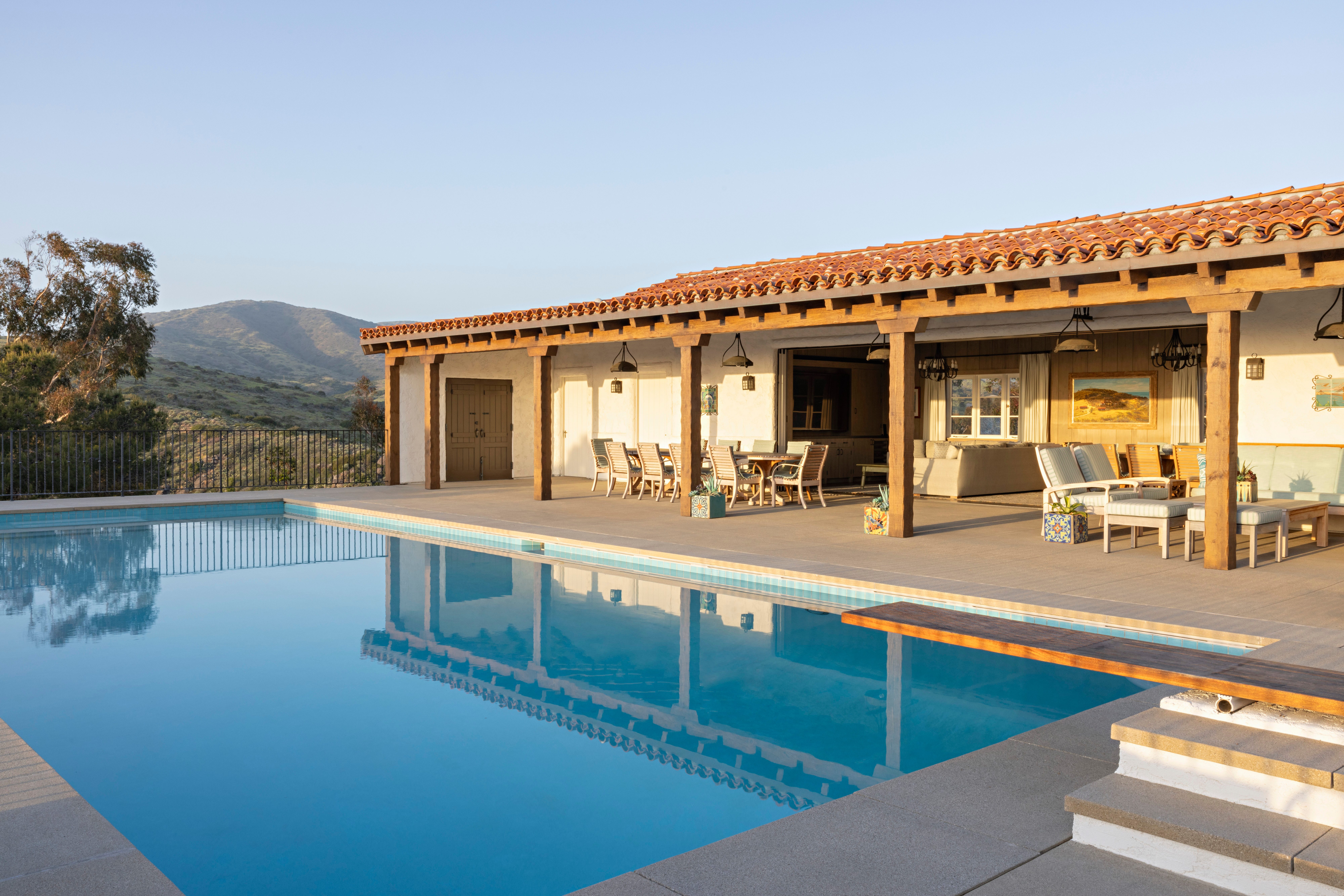 Pool with diving board beside a tile-roofed patio and hillside view at El Rancho Escondido.