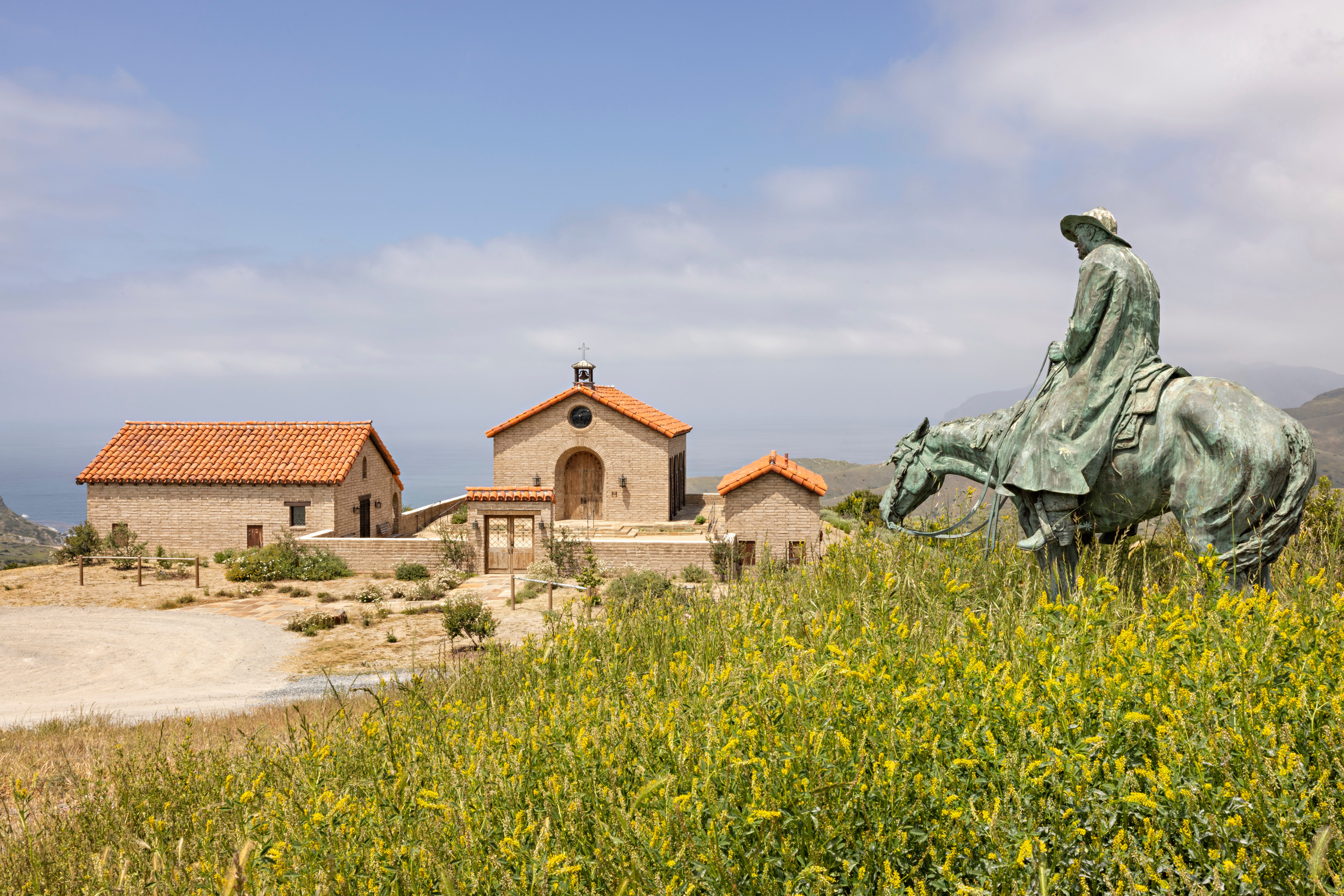 Bronze horse-and-rider statue overlooking a stone chapel and ocean at El Rancho Escondido.