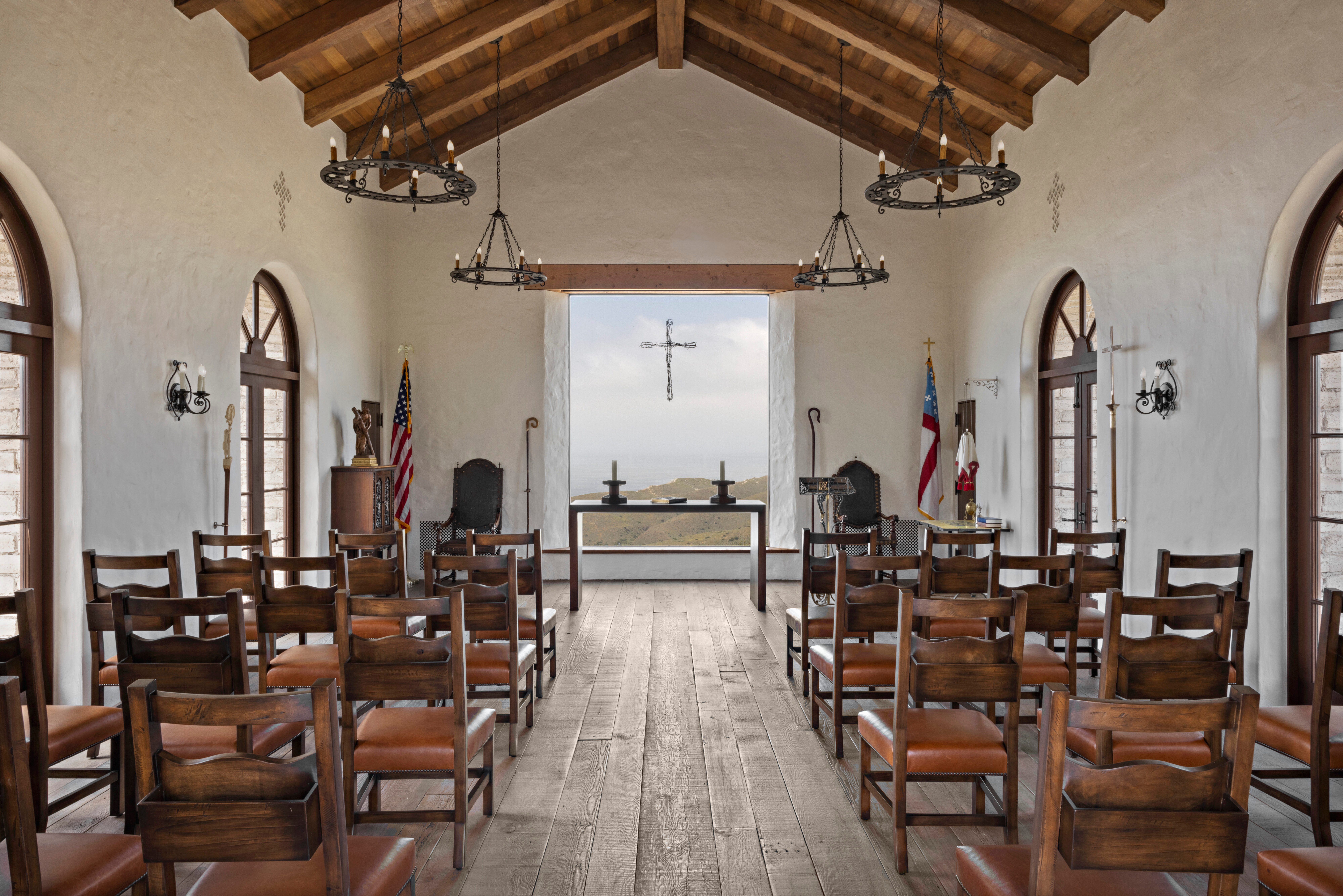 Chapel interior with wood-beam ceiling, rows of chairs, and a window overlooking mountains at El Rancho Escondido.