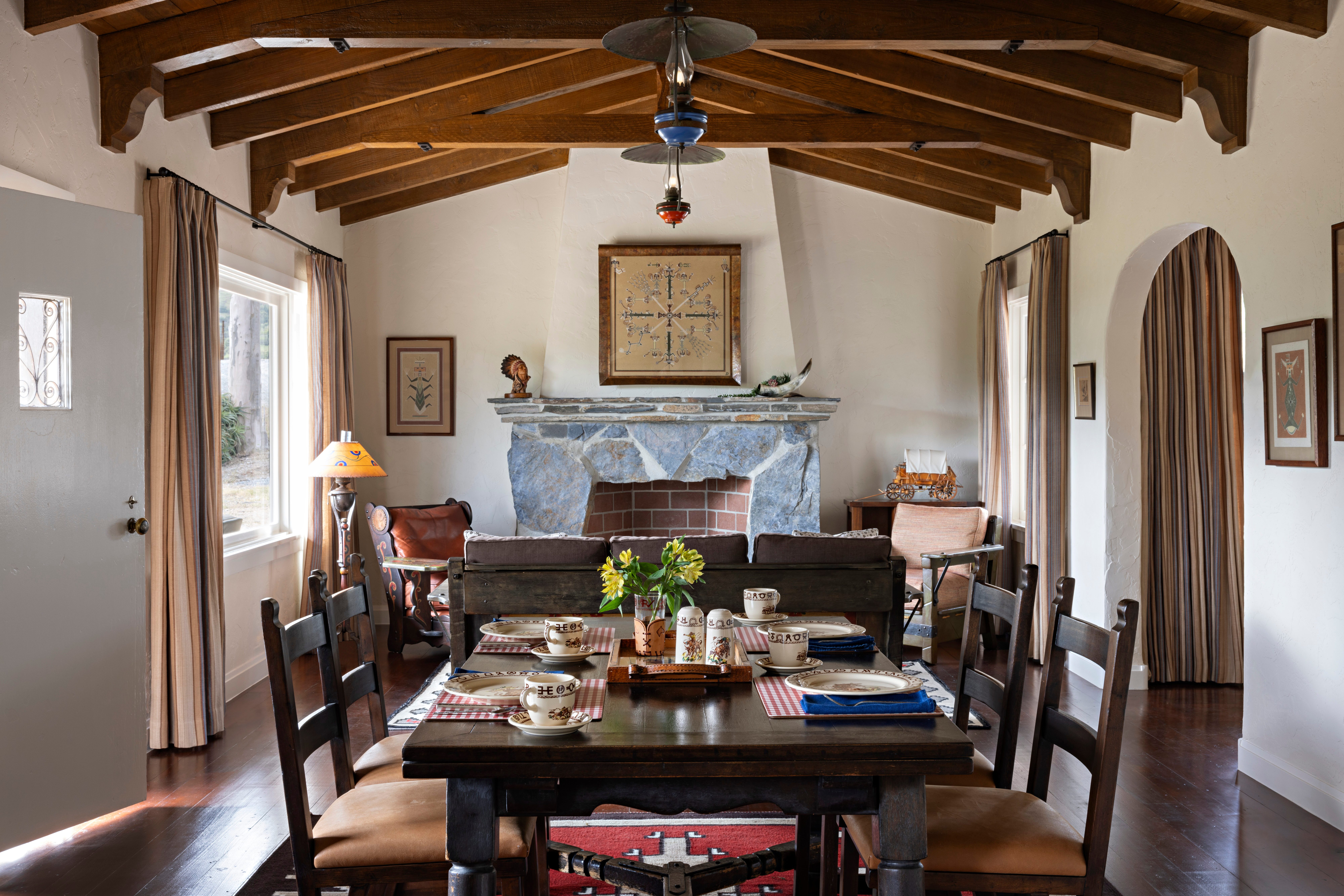 Dining room with vaulted wood-beam ceiling, set table, and stone fireplace at El Rancho Escondido.
